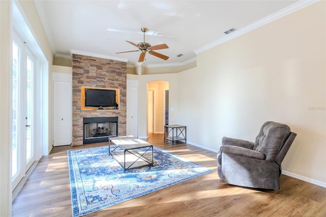 living room featuring ceiling fan, a stone fireplace, wood-type flooring, and crown molding