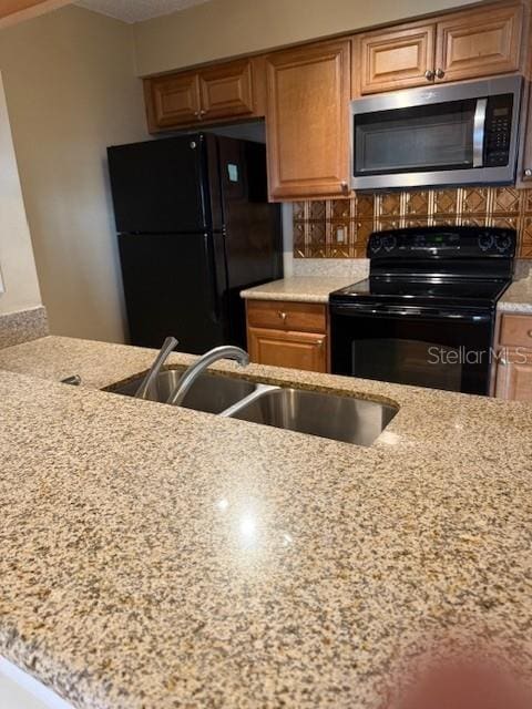 kitchen with decorative backsplash, sink, light stone counters, and black appliances