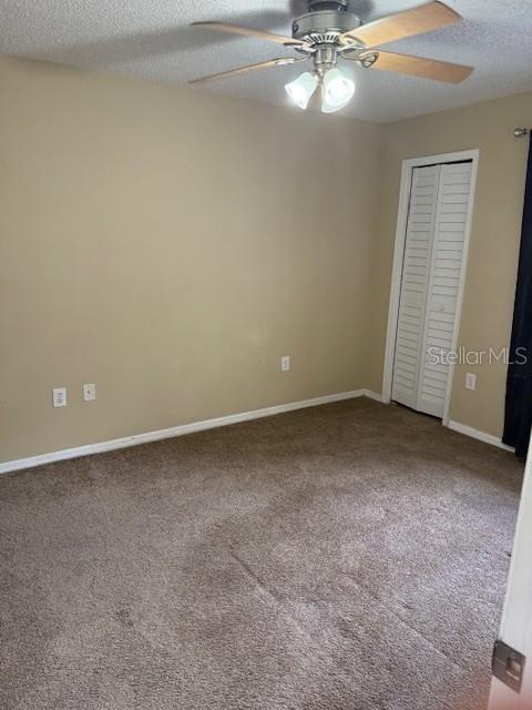 unfurnished bedroom featuring carpet, ceiling fan, a textured ceiling, and a closet