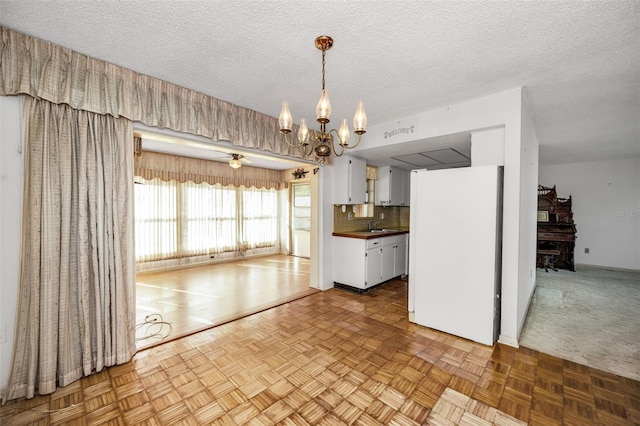 kitchen featuring ceiling fan with notable chandelier, white refrigerator, a textured ceiling, white cabinetry, and light parquet flooring