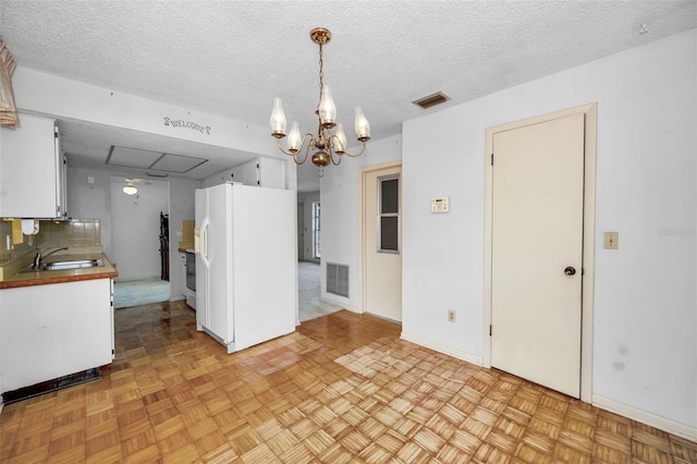 kitchen with white cabinetry, white fridge with ice dispenser, sink, hanging light fixtures, and a notable chandelier