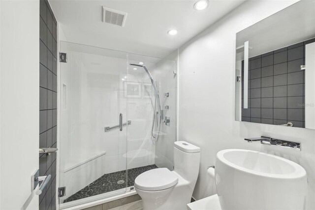 bathroom featuring toilet, a shower with shower door, and sink