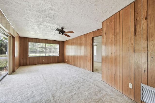 carpeted spare room featuring ceiling fan and wood walls