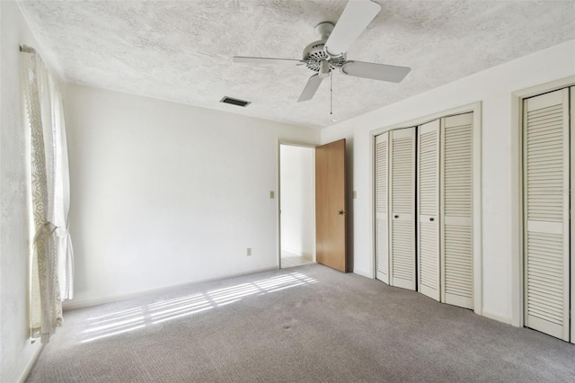 unfurnished bedroom featuring carpet flooring, a textured ceiling, ceiling fan, and multiple closets