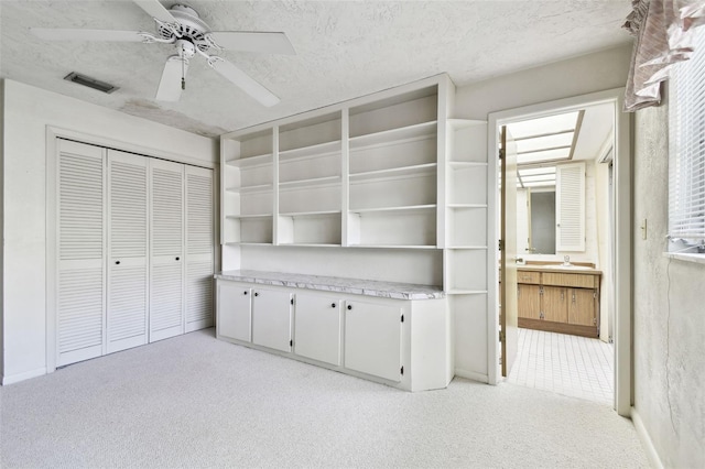 unfurnished bedroom with ceiling fan, a closet, light colored carpet, and a textured ceiling