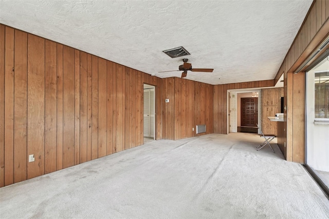 carpeted empty room featuring ceiling fan, wooden walls, and a textured ceiling