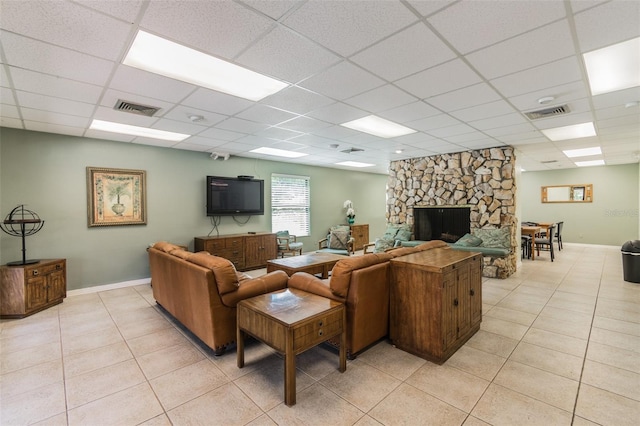 tiled living room featuring a stone fireplace and a drop ceiling