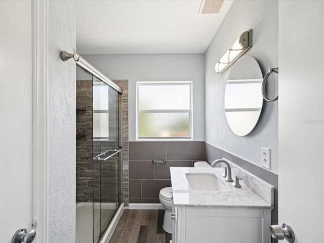 bathroom with vanity, a shower with door, hardwood / wood-style flooring, toilet, and tile walls