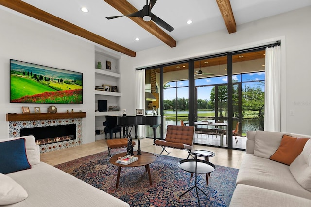 living room with a fireplace, beamed ceiling, a water view, ceiling fan, and built in shelves