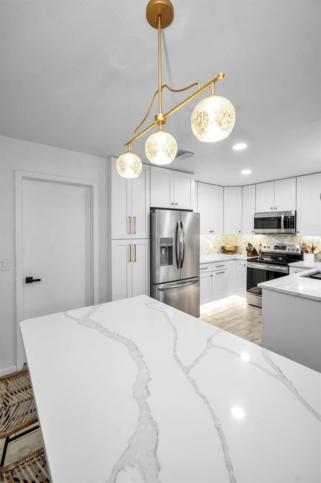 kitchen with white cabinetry, tasteful backsplash, light stone counters, pendant lighting, and appliances with stainless steel finishes