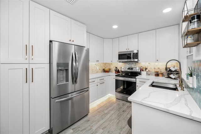 kitchen featuring sink, light stone countertops, light wood-type flooring, white cabinetry, and stainless steel appliances