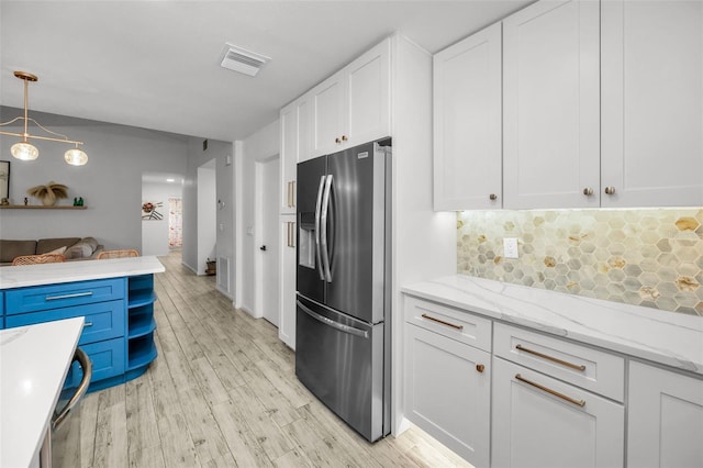 kitchen featuring white cabinetry, hanging light fixtures, light hardwood / wood-style flooring, stainless steel fridge, and decorative backsplash