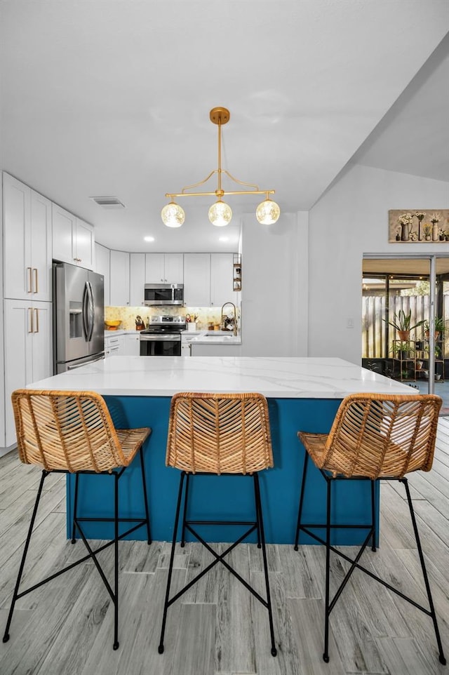 kitchen with white cabinets, a breakfast bar, pendant lighting, and appliances with stainless steel finishes