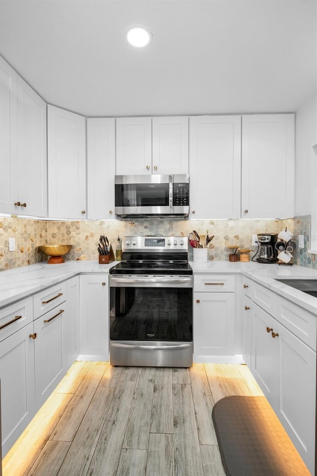 kitchen with white cabinets, tasteful backsplash, appliances with stainless steel finishes, and light hardwood / wood-style flooring