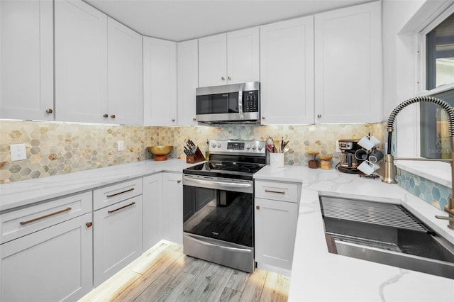 kitchen with white cabinets, appliances with stainless steel finishes, decorative backsplash, and light hardwood / wood-style flooring