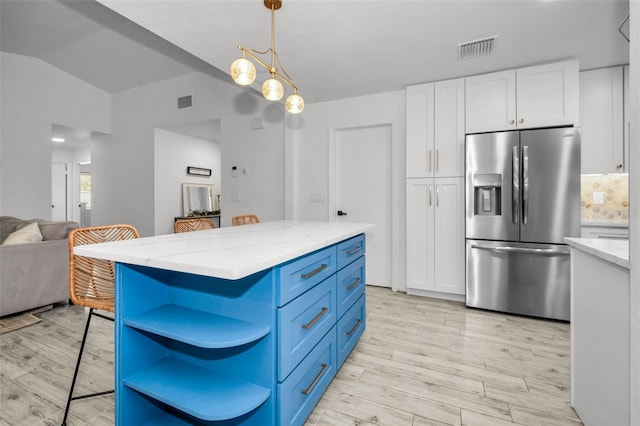 kitchen with white cabinets, stainless steel fridge, a kitchen island, and light hardwood / wood-style flooring