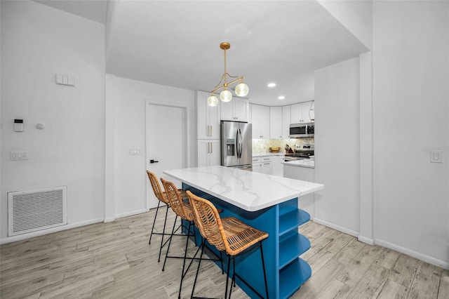 kitchen with appliances with stainless steel finishes, light wood-type flooring, light stone counters, a kitchen island, and white cabinetry