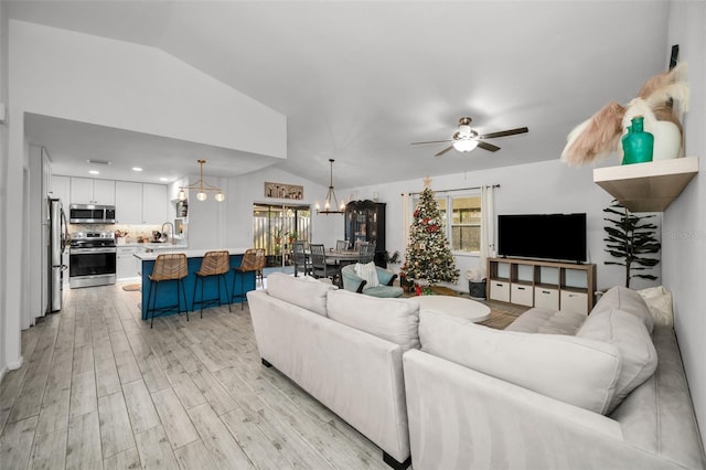 living room with ceiling fan with notable chandelier, lofted ceiling, and light hardwood / wood-style flooring