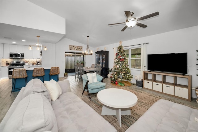 living room featuring ceiling fan with notable chandelier, light wood-type flooring, vaulted ceiling, and sink