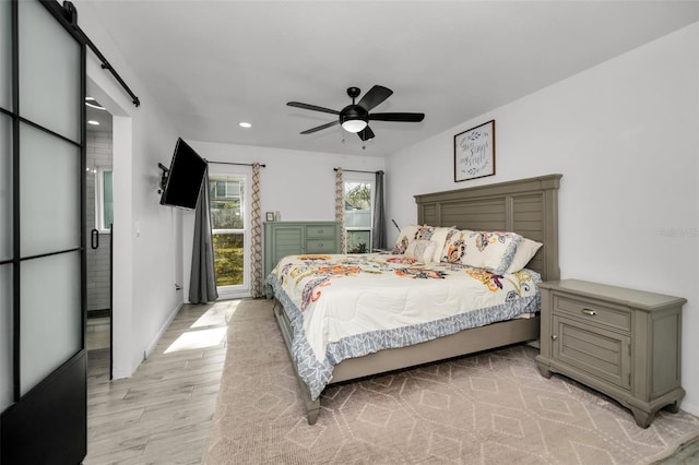 bedroom with a barn door, ceiling fan, and light wood-type flooring