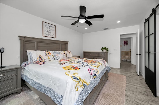 bedroom with light wood-type flooring, a barn door, and ceiling fan