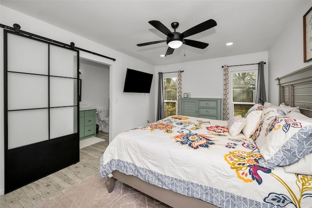 bedroom featuring ensuite bath, ceiling fan, light carpet, and a barn door