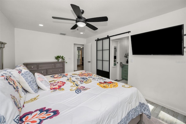 bedroom with a barn door, ceiling fan, ensuite bath, and light wood-type flooring