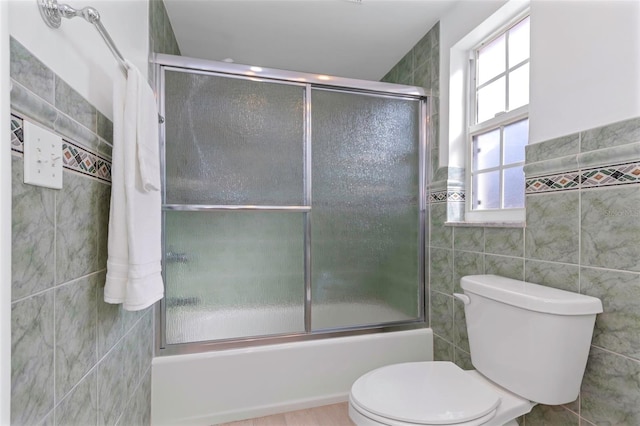 bathroom featuring toilet, bath / shower combo with glass door, and tile walls