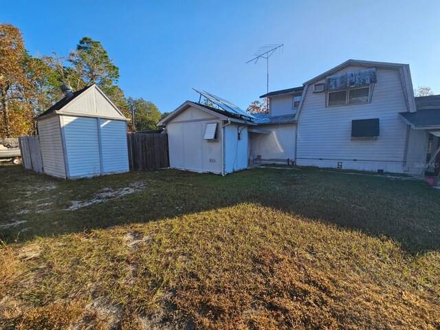 rear view of property featuring solar panels, a yard, and a storage shed