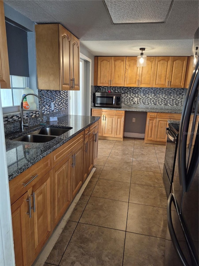 kitchen with sink, dark stone countertops, decorative backsplash, light tile patterned floors, and black appliances