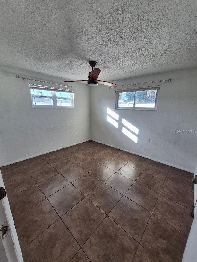 unfurnished room featuring a textured ceiling, dark tile patterned floors, plenty of natural light, and ceiling fan