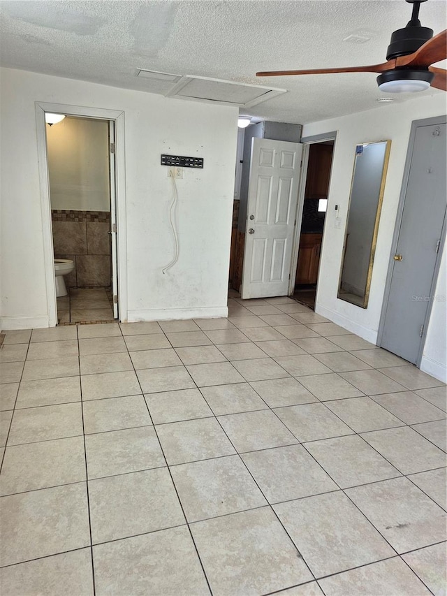 empty room featuring ceiling fan, light tile patterned floors, and a textured ceiling