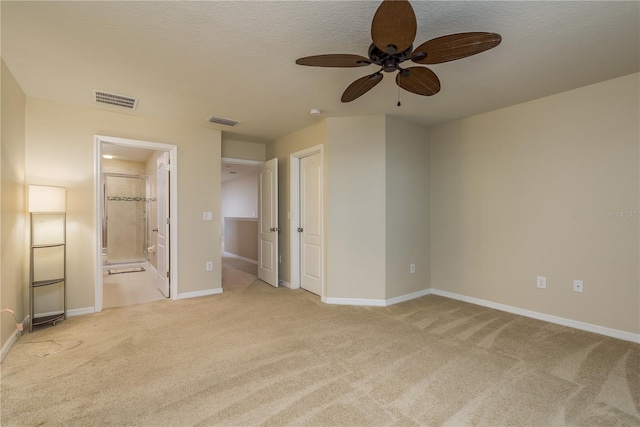 unfurnished bedroom featuring ensuite bathroom, a textured ceiling, ceiling fan, and light colored carpet