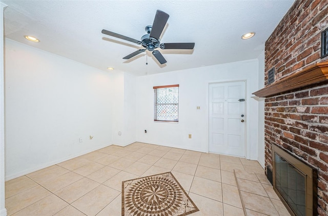 unfurnished living room with ceiling fan, a fireplace, light tile patterned floors, and a textured ceiling