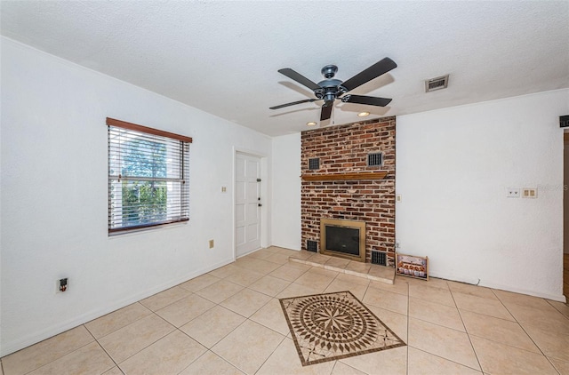 unfurnished living room featuring ceiling fan, light tile patterned floors, a textured ceiling, and a brick fireplace