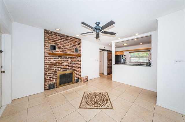 unfurnished living room featuring a brick fireplace, a textured ceiling, ceiling fan, sink, and light tile patterned floors