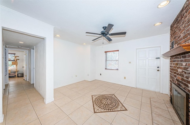 unfurnished living room featuring ceiling fan, light tile patterned floors, a textured ceiling, and a brick fireplace