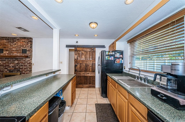 kitchen featuring sink, a barn door, a textured ceiling, light tile patterned floors, and black appliances