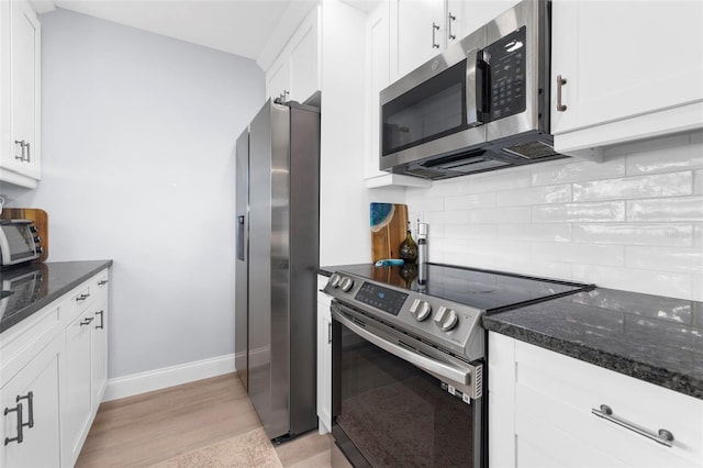 kitchen with stainless steel appliances, backsplash, dark stone countertops, white cabinets, and light wood-type flooring