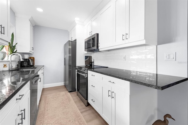 kitchen with white cabinets, sink, dark stone countertops, light wood-type flooring, and stainless steel appliances