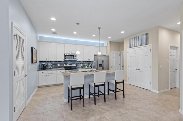 kitchen with light stone counters, an island with sink, pendant lighting, stainless steel appliances, and white cabinets