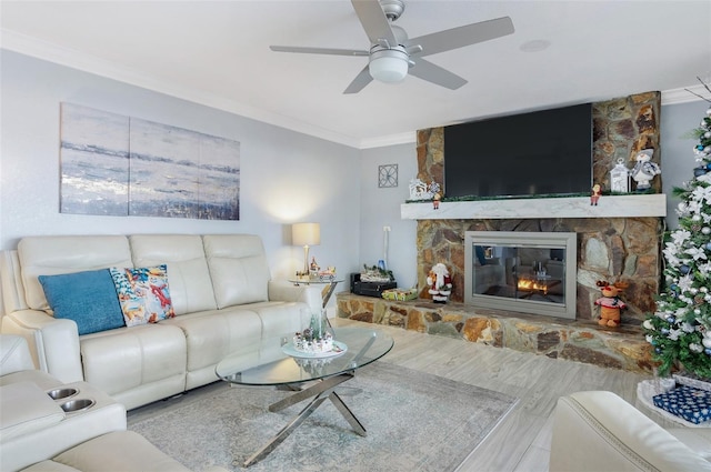 living room featuring hardwood / wood-style flooring, a stone fireplace, ceiling fan, and ornamental molding