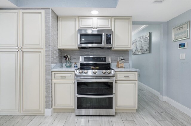 kitchen featuring light countertops, decorative backsplash, appliances with stainless steel finishes, and baseboards