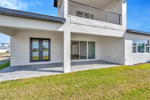 back of house featuring french doors, a balcony, a patio area, and a lawn