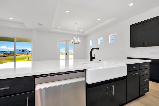 kitchen featuring dishwasher, sink, a tray ceiling, decorative light fixtures, and light hardwood / wood-style floors