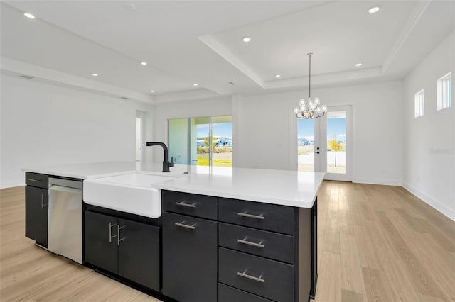 kitchen with a tray ceiling, light hardwood / wood-style flooring, an island with sink, and pendant lighting