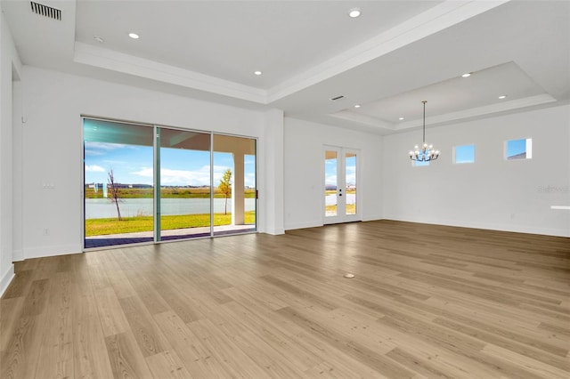 unfurnished living room featuring french doors, a tray ceiling, a water view, light hardwood / wood-style flooring, and a chandelier