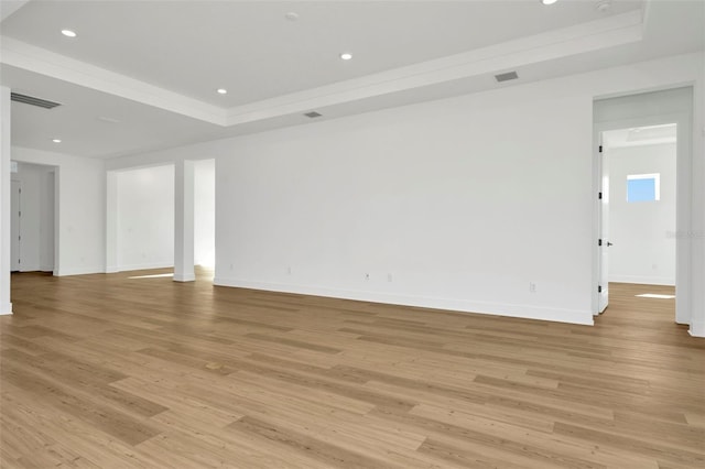 empty room with light wood-type flooring and a tray ceiling