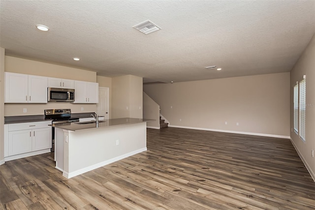 kitchen with stainless steel appliances, dark hardwood / wood-style floors, and a center island with sink