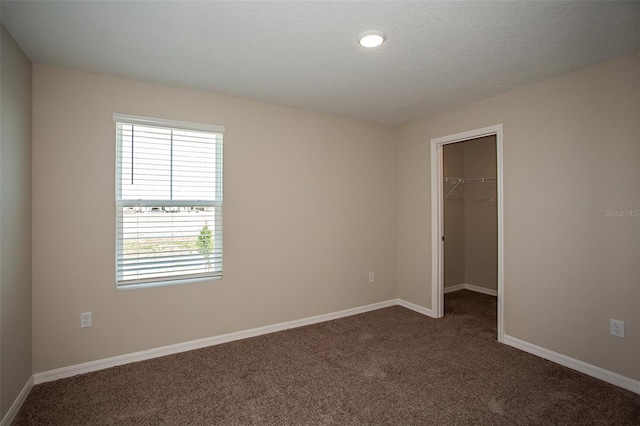 unfurnished bedroom with a walk in closet, a closet, dark carpet, and a textured ceiling